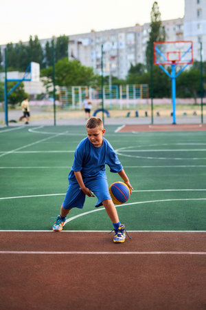 Sports and basketball. Boy in a blue tracksuit playing basketball, leading the ball. Residential urban area in the background. Copy spaceの写真素材
