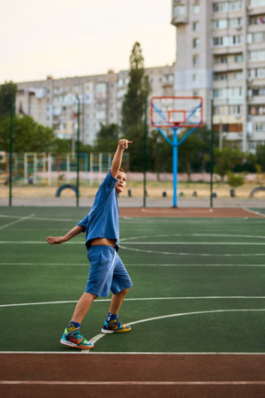 Sports and basketball. Boy in a blue tracksuit throwing a basketball ball into the hoop while playing on an outdoor court. Residential urban area in the background. Sports conceptの写真素材