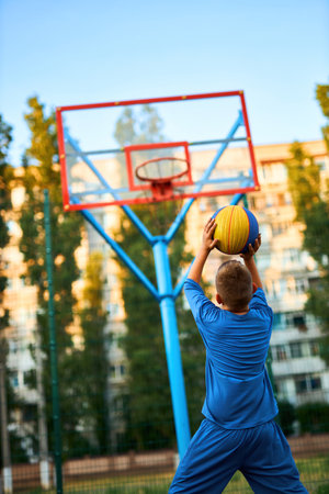 Back view of a young sporty boy shooting a basketball toward a hoop. Vertically framed shot.の写真素材