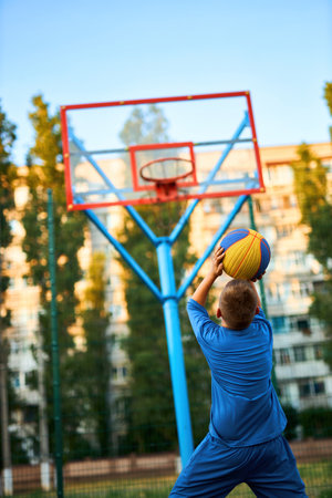 Back view of a young sporty boy shooting a basketball toward a hoop. Vertically framed shot.の写真素材