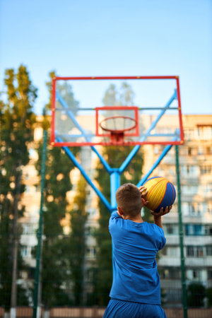 Back view of a young sporty boy shooting a basketball toward a hoop. Vertically framed shot.の写真素材