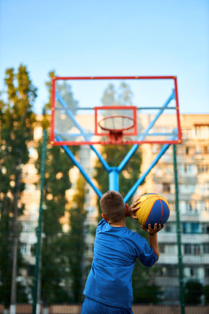 Back view of a young sporty boy shooting a basketball toward a hoop. Vertically framed shot.の写真素材
