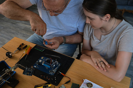 Grandfather and granddaughter work together on an electronics project at a table. Ideal for family,...