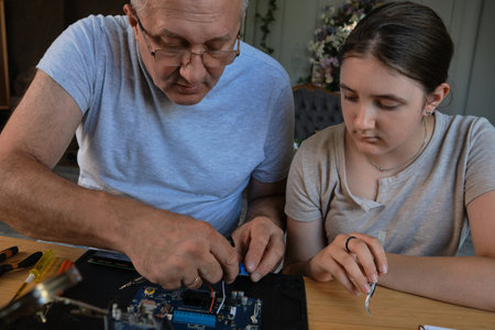 Grandfather and granddaughter work together on an electronics project at a table. Ideal for family, education, and DIY themesの写真素材