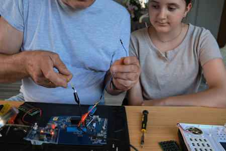 Grandfather and granddaughter work together on an electronics project at a table. Ideal for family, education, and DIY themesの写真素材