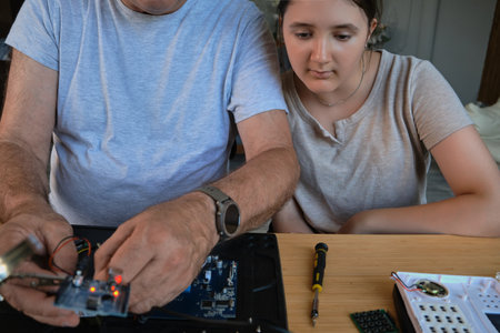 Grandfather and granddaughter work together on an electronics project at a table. Ideal for family, education, and DIY themesの写真素材