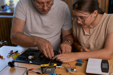 Grandfather and granddaughter work together on an electronics project at a table. Ideal for family, education, and DIY themesの写真素材