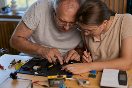 Grandfather and granddaughter work together on an electronics project at a table. Ideal for family, education, and DIY themesの写真素材