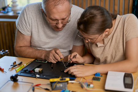 Grandfather and granddaughter work together on an electronics project at a table. Ideal for family, education, and DIY themesの写真素材
