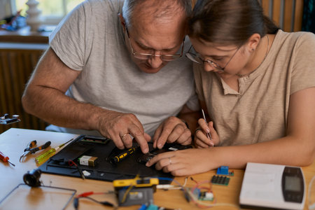 Grandfather and granddaughter work together on an electronics project at a table. Ideal for family, education, and DIY themesの写真素材