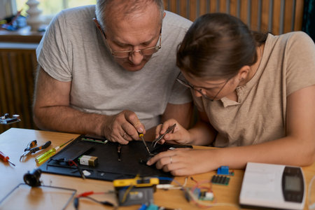 Grandfather and granddaughter work together on an electronics project at a table. Ideal for family, education, and DIY themesの写真素材