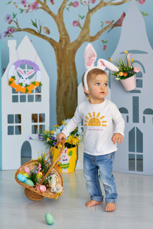 Beautiful child with painting eggs. Happy family preparing for Easter. Cute little girl is wearing...