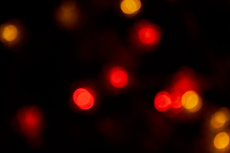 Defocused bokeh red big lights on black background. Blurred abstract red glitter wallpaper for love theme, Valentine's day.の写真素材