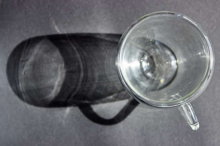 A long gray shadow from a transparent glass cup. Dark gray abstract background for design, social networks with space for text. Top view.の写真素材