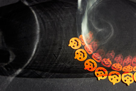 Bright orange little pumpkin stickers are reflected by scary shadows in a glass glass. Bright orange Halloween pumpkins on a dark gray background. Design background with space for text on the left. Top view.の写真素材