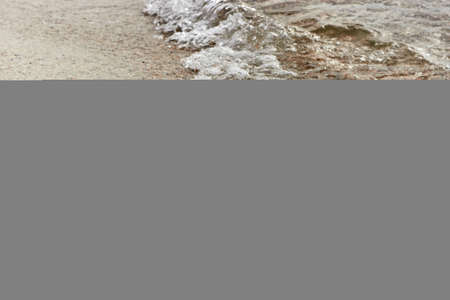 A small sea wave with foam. Sea foam on beach sand with clear water. Sand Beach And Sea Foam Macro...
