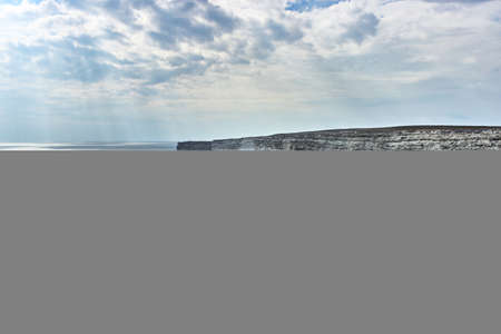 Cape by the sea. Seascape, horizon, calm blue-gray sea. Bad weather, impending clouds, the sun's...
