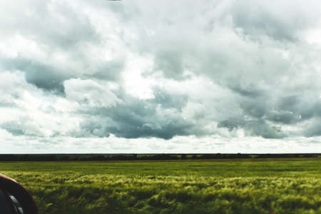 View from the side window of the car on a beautiful landscape. Green fields, trees, heavy gray clouds.の写真素材