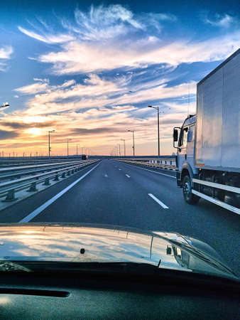 View from the car's windshield to a beautiful sunset, a large highway, a truck. Traveling by car. Beautiful blue-orange sky at sunset.の写真素材