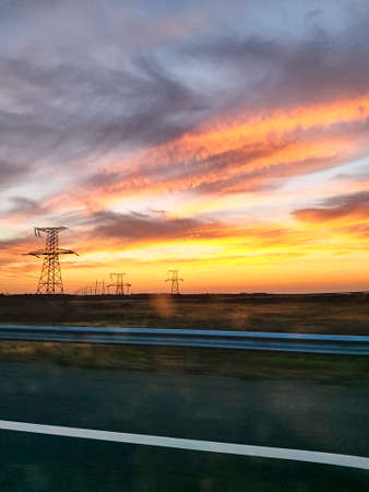 View from the windshield of the car on a beautiful sunset, a large highway. Traveling by car. Beautiful orange sky at sunset over the power lines.の写真素材