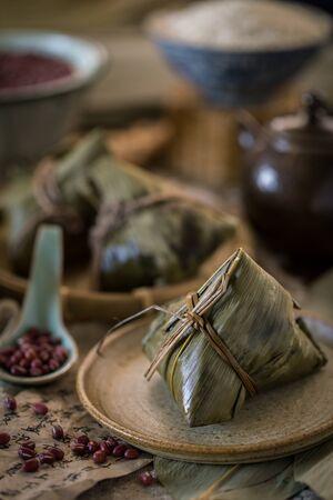 Glutinous rice dumplings with red bean azuki bean wrapped with bamboo leaves with traditional Chinese style setting as backgroundの写真素材