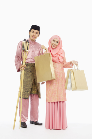 Husband and wife in traditional Malay clothes with shopping bags and Pelita torchの写真素材