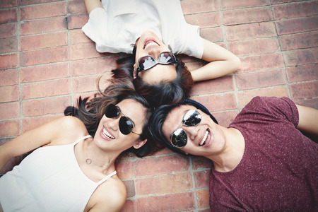 Friends laughing together while lying down on the floor at a parkの写真素材