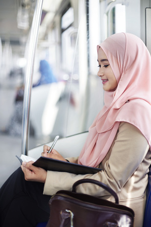 Young Malay woman writing notes in a trainの写真素材