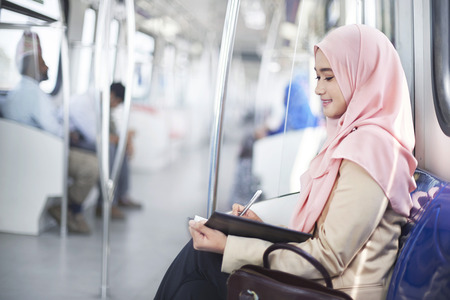 Young Malay woman writing notes in a trainの写真素材
