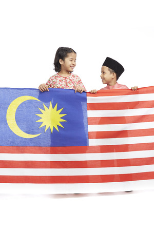 Boy and girl in traditional Malay clothes holding Malaysian country flagの写真素材