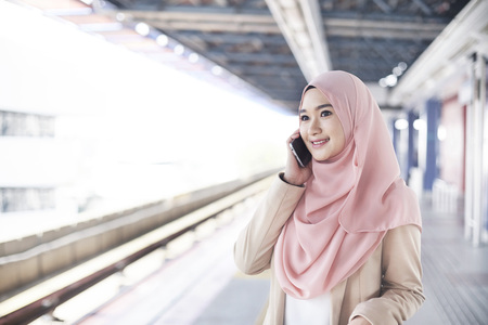Young Malay woman talking on the phone beside train platformの写真素材