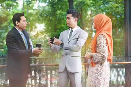 Businessman drinking coffee while businesswoman standing nearby