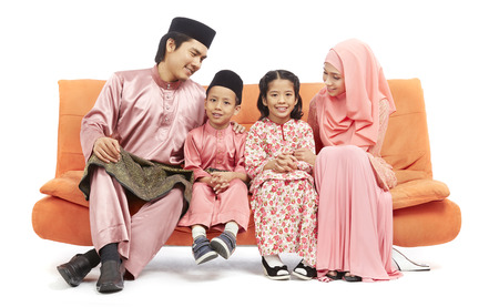 Family in traditional Malay clothes sitting on sofa seatの写真素材
