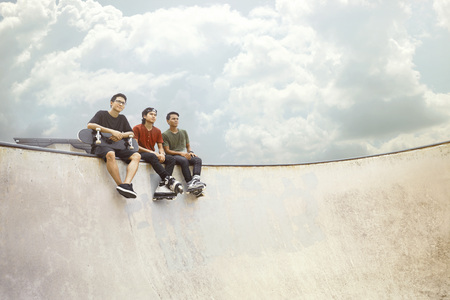 Young men sitting on the edge of ramp at a skate parkの写真素材