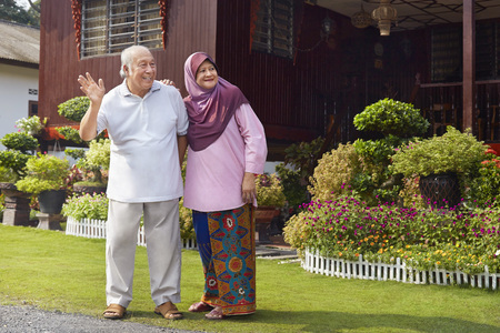 Senior couple smiling and waving in front of wooden houseの写真素材