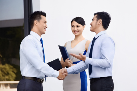 Two businessmen shaking hands while businesswoman stands nearbyの写真素材