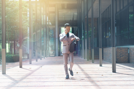Young businessman talking on the phone while looking at his watchの写真素材