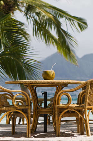 Refreshing coconut drink in the shell sitting atop a bamboo table on a tropical beach.の写真素材