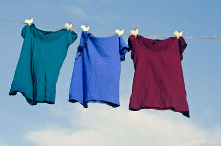 A group of female t-shirts hanging on string against blue sky.の写真素材