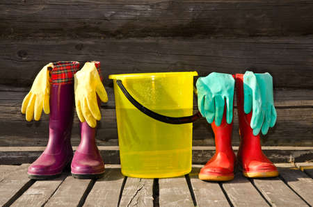 Bucket, rubber gloves and two pairs of rubber boots at sunny wooden verandaの写真素材