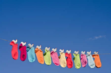 String of colorful socks on a rope against sunny blue sky in the garden の写真素材
