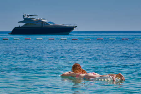 Young Woman on Inflatable Matress looking at Yacht Boat at Seaの写真素材
