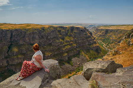 Young woman sitting on the edge of Kasagh river gorge near Saghmosavank monasteryの写真素材