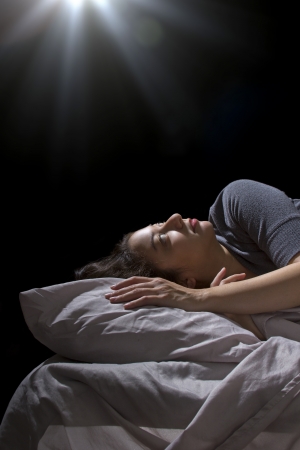 creepy glowing orb hovering over a woman sleeping in bedの写真素材