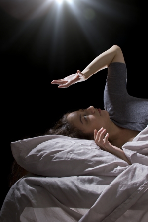creepy glowing orb hovering over a woman sleeping in bedの写真素材