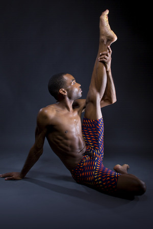 fit and slim black male doing yoga stretches on grey backgroundの写真素材