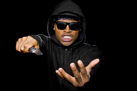 thug wearing a hoodie and holding a knife coming out of the shadows