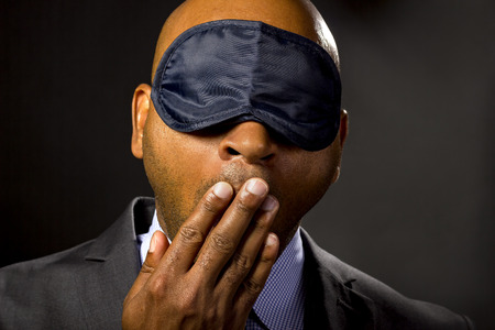 Sleepy businessman wearing an eye mask because of jet lagの写真素材