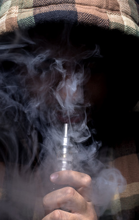 Man with concealed identity smoking a controversial vape is a health riskの写真素材