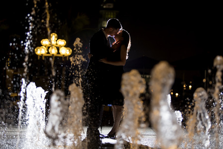 Engaged interracial couple on a romantic date at night on a city fountainの写真素材